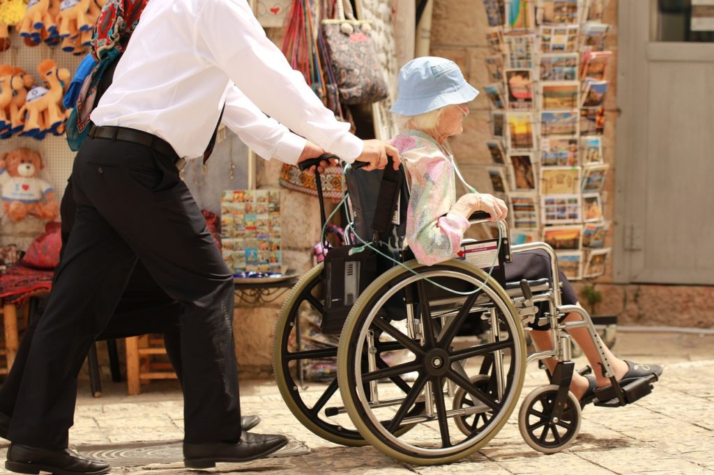 Uomo spinge donna anziana su sedia a rotelle