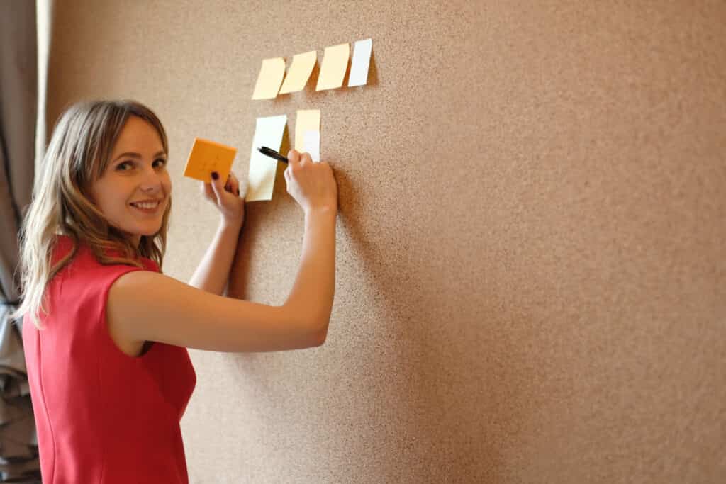 Donna che appende post-it su una parete in sughero