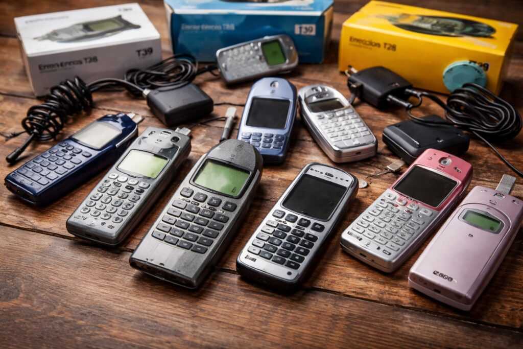 Collezione di vecchi telefoni Ericsson e Sony Ericsson appoggiati su un tavolo in legno, con modelli storici e accessori originali ben visibili.