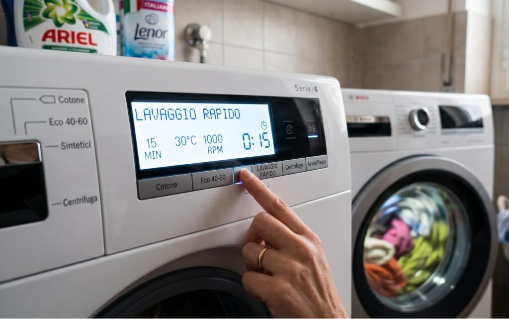 Dito indice che preme il pulsante del lavaggio rapido sul display digitale luminoso di una lavatrice moderna durante un ciclo domestico