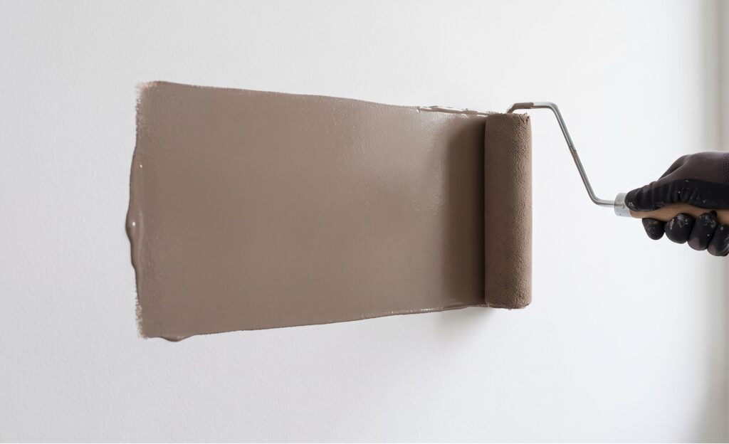 Un rullo da imbianchino carico di pittura color tortora che scorre in modo fluido su una parete bianca senza lasciare righe o striature di colore.