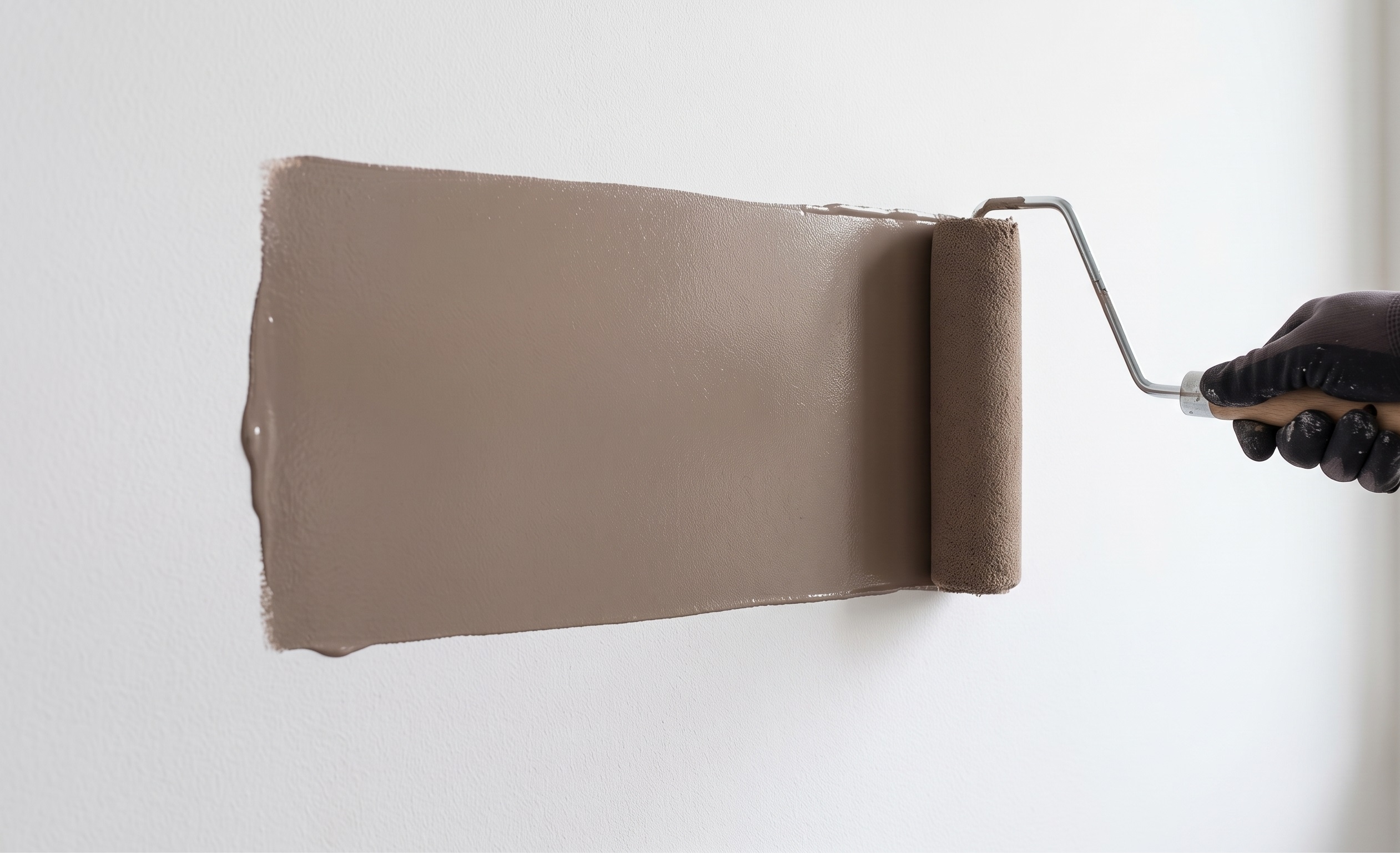 Un rullo da imbianchino carico di pittura color tortora che scorre in modo fluido su una parete bianca senza lasciare righe o striature di colore.