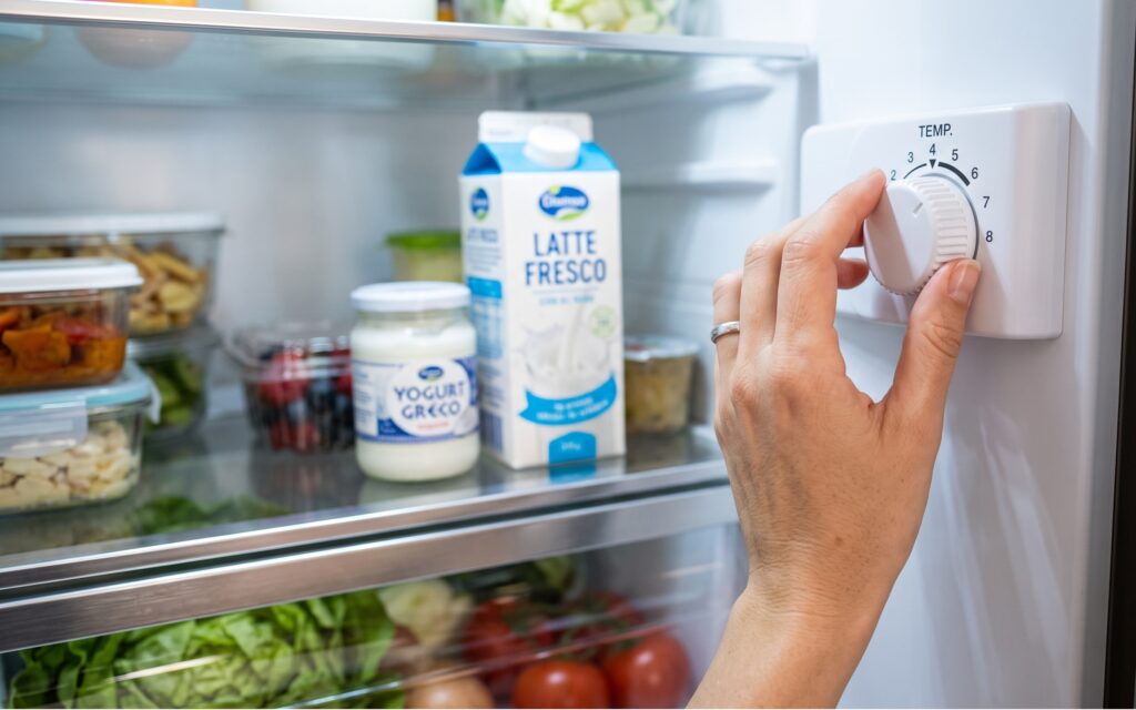 una mano che regola la manopola interna della temperatura di un frigorifero moderno